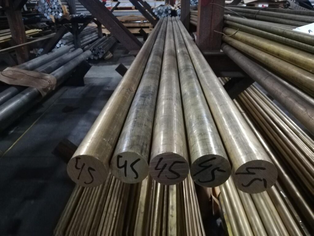 Batang perunggu diameter 45–51 mm tersusun rapi di gudang, siap untuk kebutuhan industri dan pemesinan presisi.